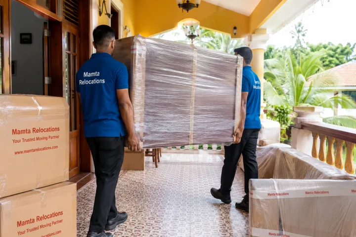Uniformed Mamta Relocations movers carrying wrapped cabinets through the breezy veranda of a Goan villa, every item fully wrapped and protected
