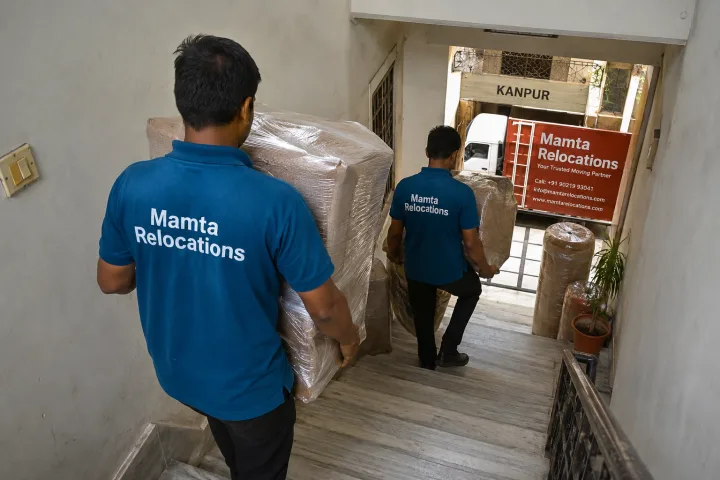 Uniformed Mamta Relocations movers carrying wrapped goods down the narrow staircase of a Kanpur house, every item fully wrapped and protected