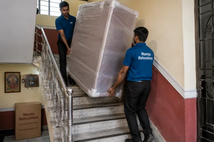 Uniformed Mamta Relocations movers carrying a wrapped almirah down the staircase of a Patna house, every item fully wrapped and protected