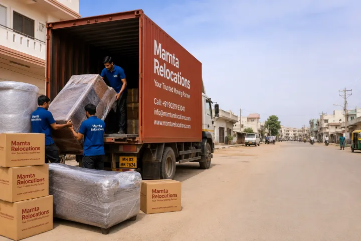 Mamta Relocations crew loading stretch-wrapped furniture and labelled cartons into their truck on a dusty Rajkot road in a mid-size Gujarati