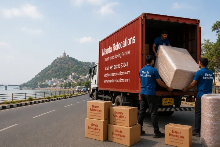 Mamta Relocations crew loading stretch-wrapped furniture and labelled cartons into their truck on a Vijayawada road with the Kanaka Durga hill